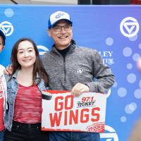 Three alumni pose together with a "Go Wings" sign at the Detroit Red Wings GVSU Night